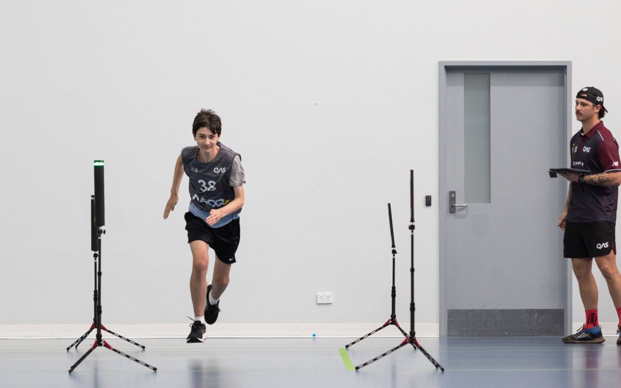 Young male athlete running with talent team advisor watching from the side.