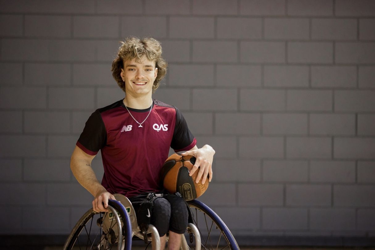 Eithen smiles while holding a basketball wearing a QAS shirt