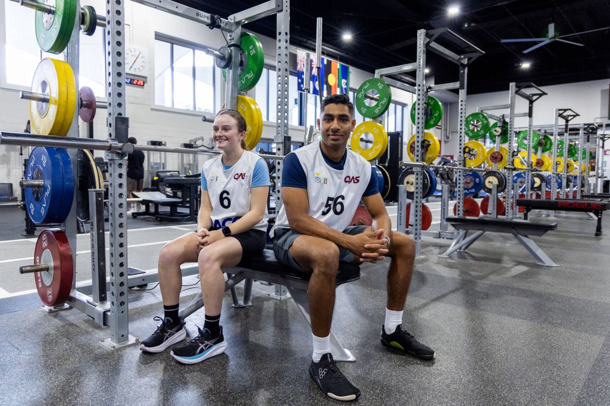 Two athletes sitting on bench surrounding by gym equipment at the QAS