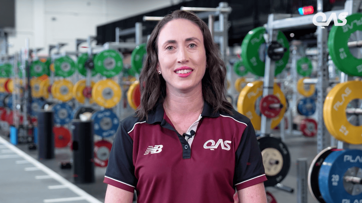 woman smiling in a gym, surrounded by weightlifting equipment