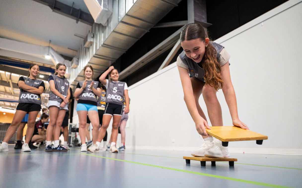 Young girl putting timber blocks down on floor, with a group of young girls around her.