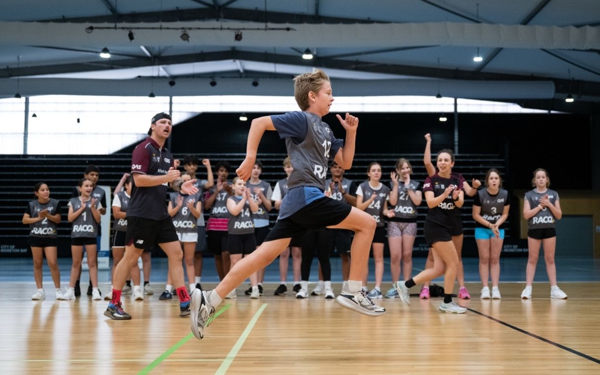 Young boy running with a crowd of children cheering him on alongside two YouFor2032 Talent Team advisors.