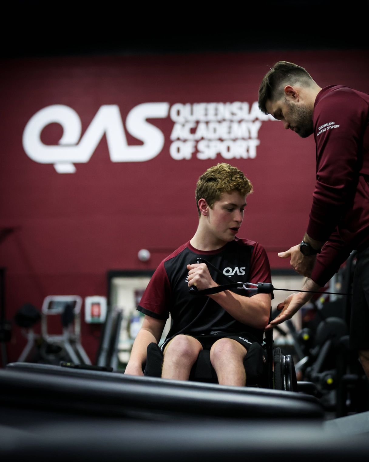 A Para Unit athlete in a wheelchair is supported by a strength and conditioning coach to complete a gym exercise.