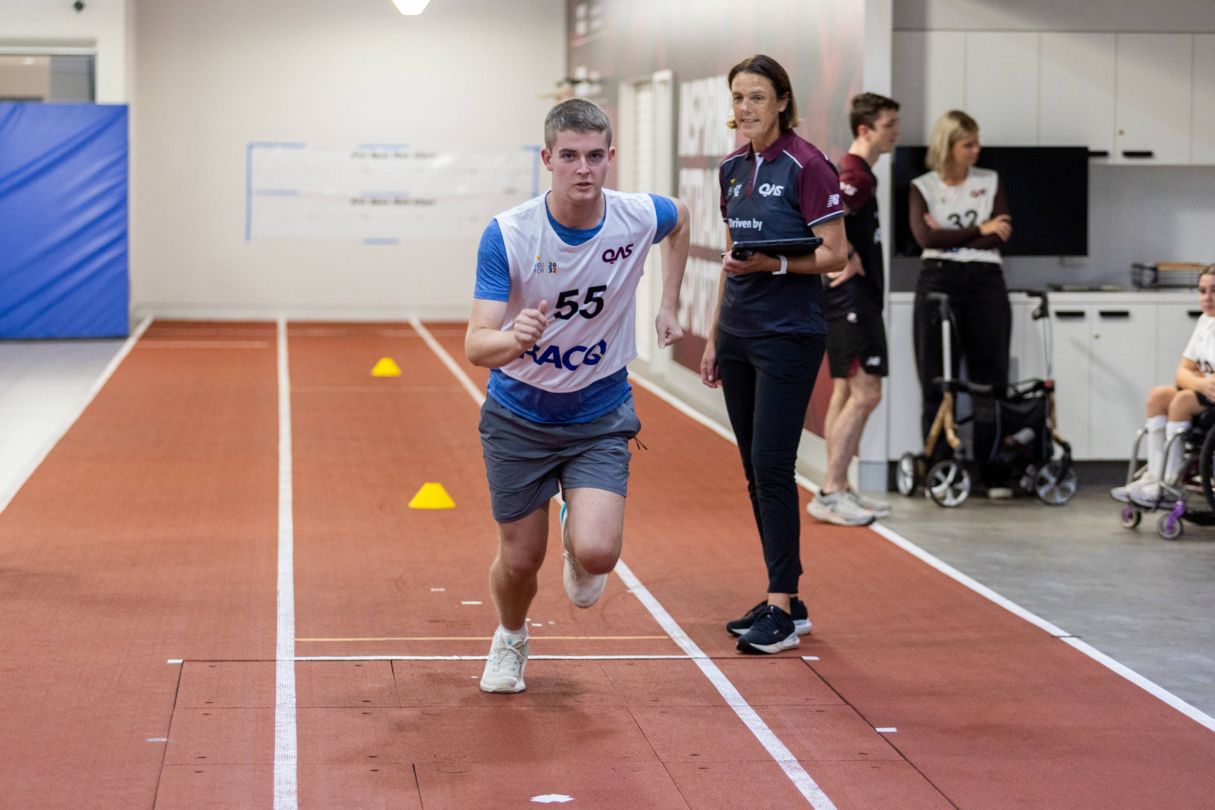 Young male athlete running with a YouFor2032 Talent Advisor watching.