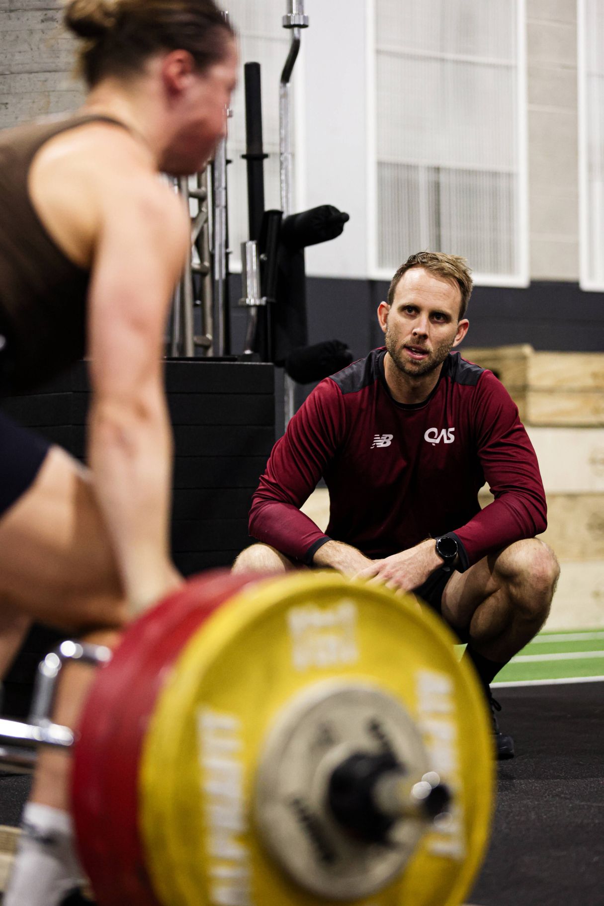 Athlete in gym lifting weights supported by QAS Performance Support team member.