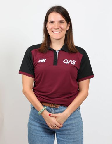 Female wearing a maroon QAS shirt, crossing hands and wearing denim blue jeans.